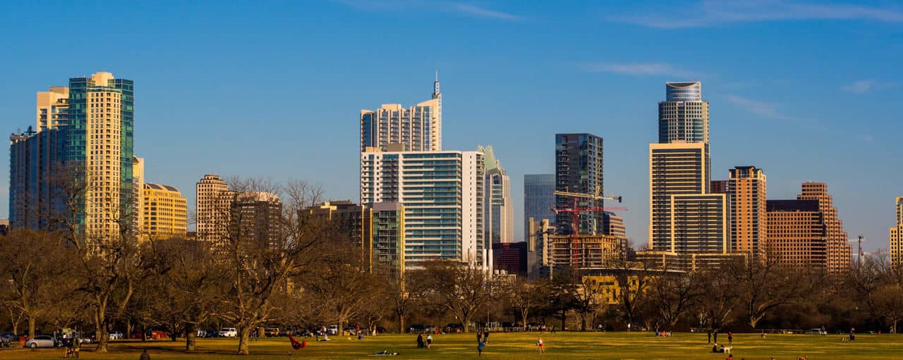 City skyline of modern buildings near Zilker/Bouldin Creek in Texas, with a park in the foreground and blue sky.