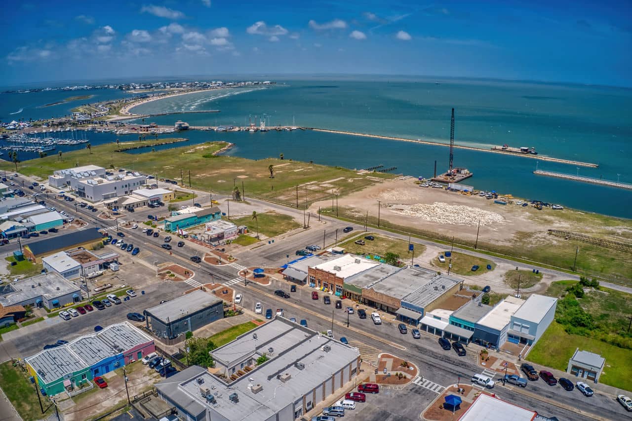 Aerial view of North Beach/Rockport, Texas, showing colorful buildings, streets, and a marina along the coastline.