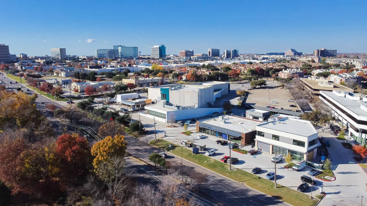 Aerial view of the Far North/Addison neighborhood in Texas, featuring buildings, trees, and clear blue skies.