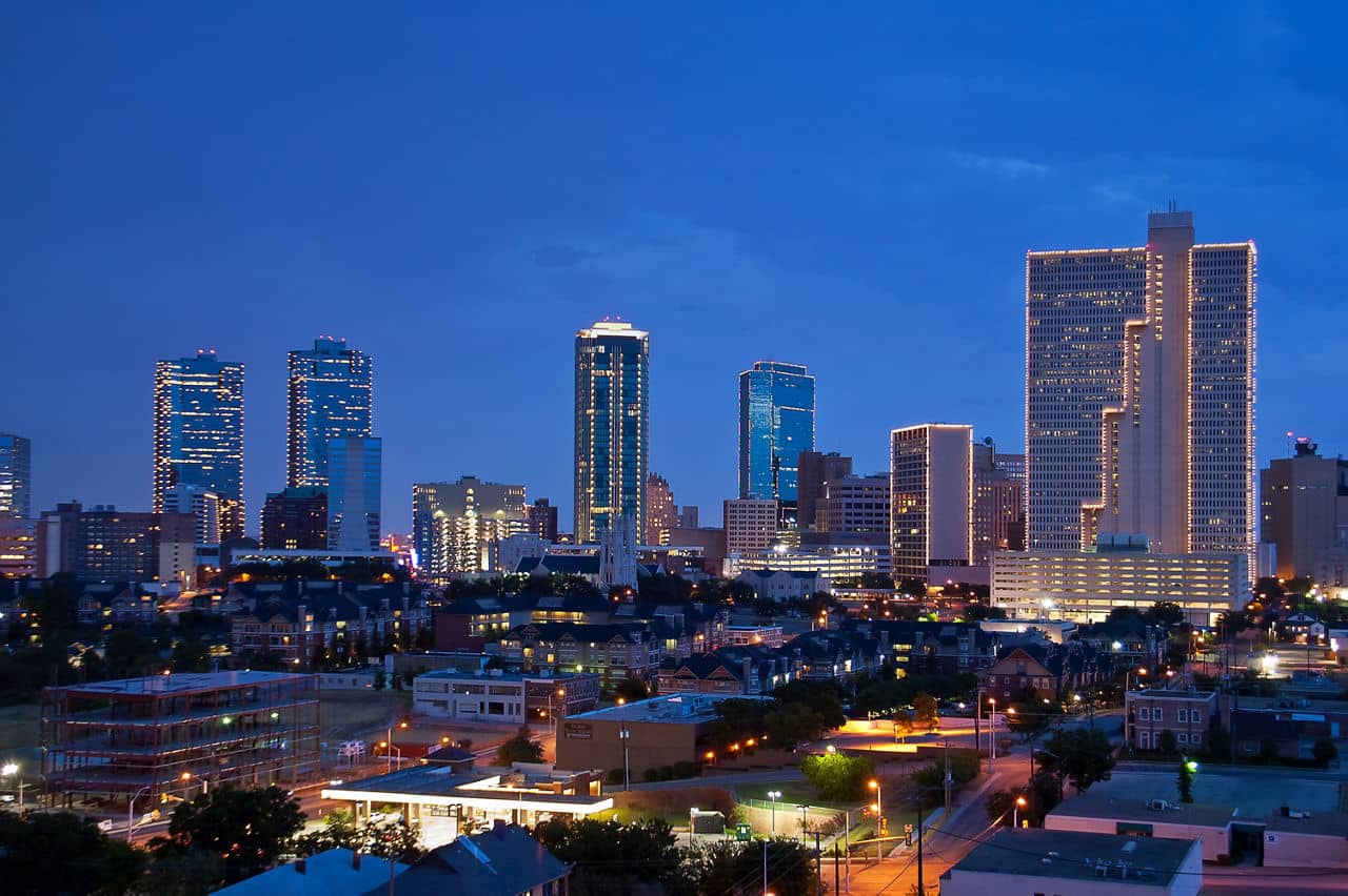 A skyline view of Fort Worth, Texas, at dusk, featuring brightly lit buildings against a darkening sky.