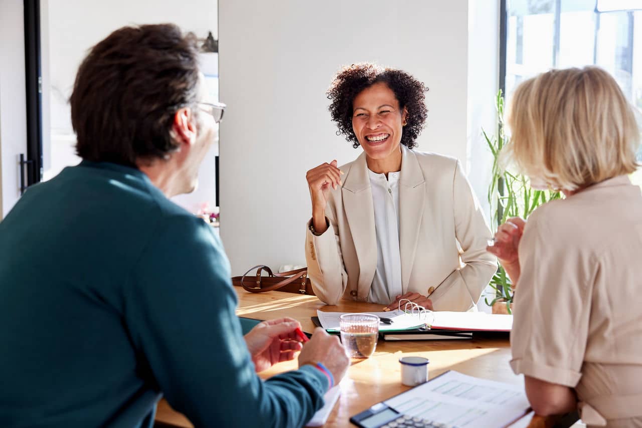 Smiling financial advisor manager speaking with couple while sitting at table and discussing home loan insurance policy